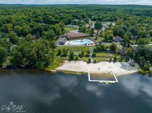 An aerial view of a resort with a swimming pool, a beach, and a dock.