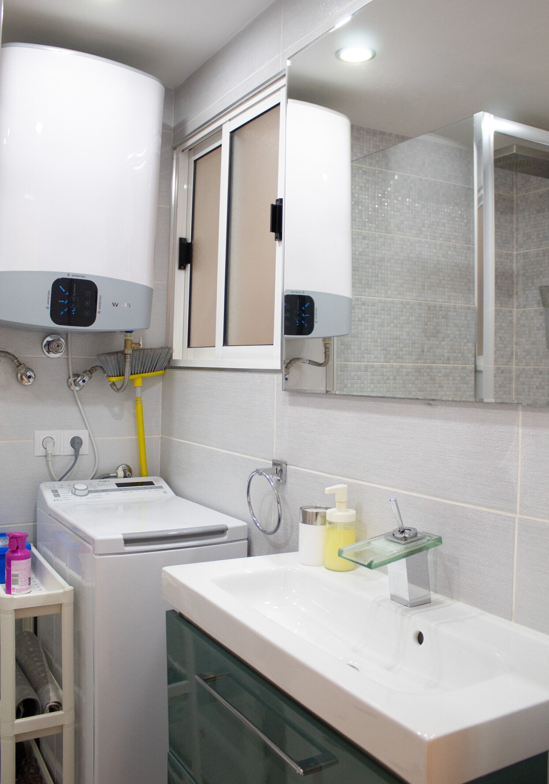 A modern bathroom with a built-in washer and dryer, a glass shower enclosure, and a white sink with a soap dispenser.