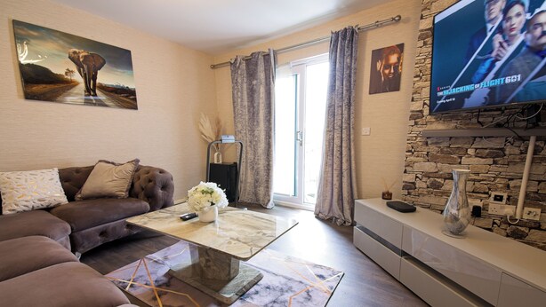 A living room with a sofa, a coffee table, a TV, and a stone wall. - Manchester Retreat - Modern 2Br Apartment (Manchester)