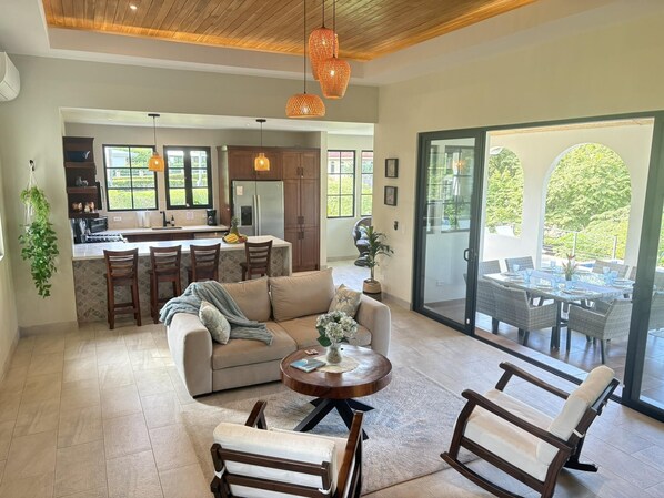 A spacious living area with a sofa, chairs, and a coffee table. A kitchen with a refrigerator and cabinets is visible in the background.