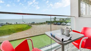 Ein Balkon mit Tisch, Stühlen und Blick auf das Meer und geparkte Autos.