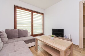 A modern living room with a sofa, a wooden coffee table, a television, and a small plant.