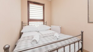 A neatly made bed with a metal frame, a window with blinds, and a radiator on the wall. - Jaglana Deluxe by Grand Apartments (Gdansk)