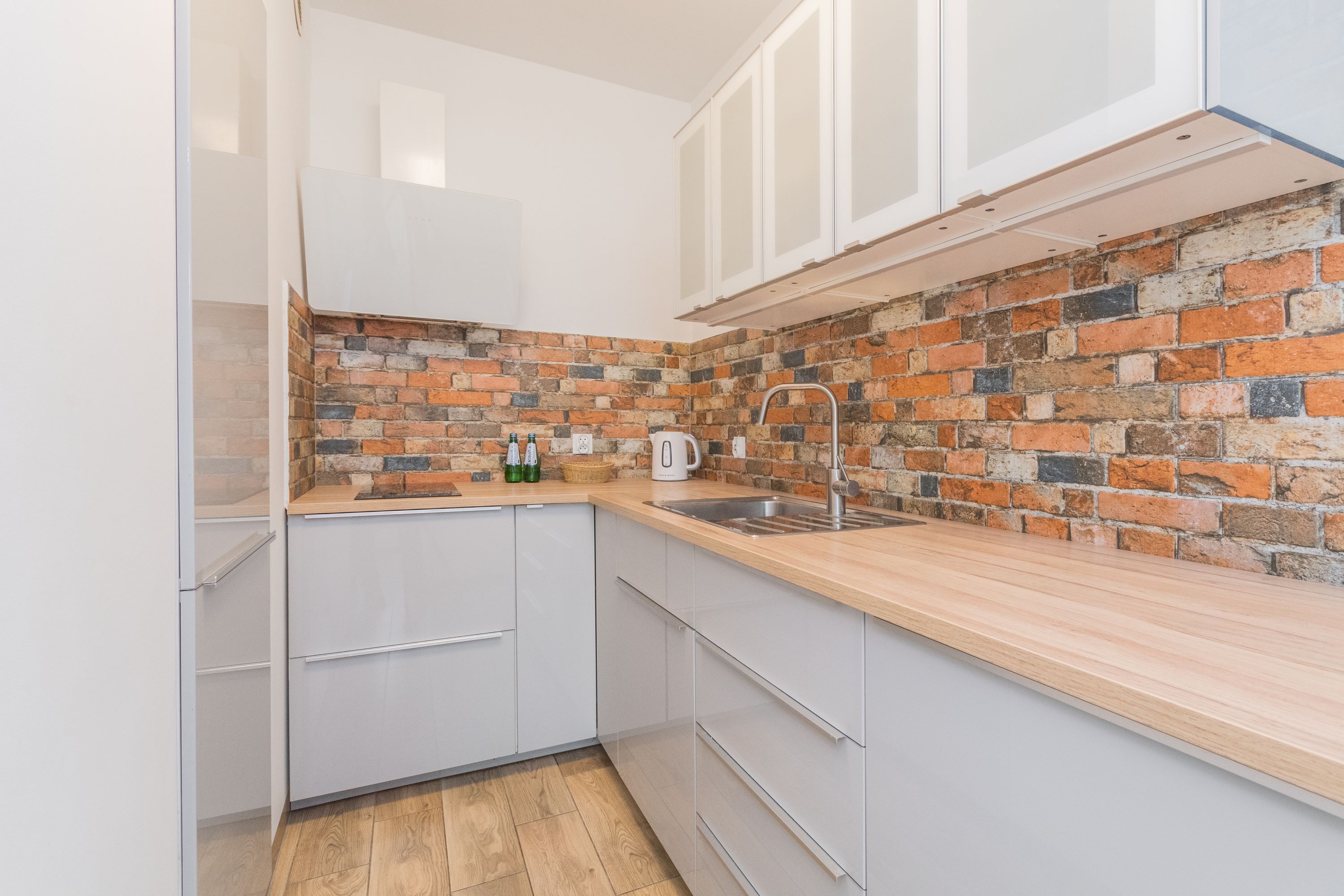 A kitchen with white cabinets, a brick backsplash, and a wooden countertop.
