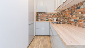 A compact kitchen with a brick backsplash, white cabinets, and a wooden countertop. - Jaglana Deluxe by Grand Apartments (Gdansk)