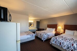 Ein Hotelzimmer mit zwei Betten, einem Kühlschrank, einem Schreibtisch, einem Spiegel und einem Nachttisch mit Lampe.