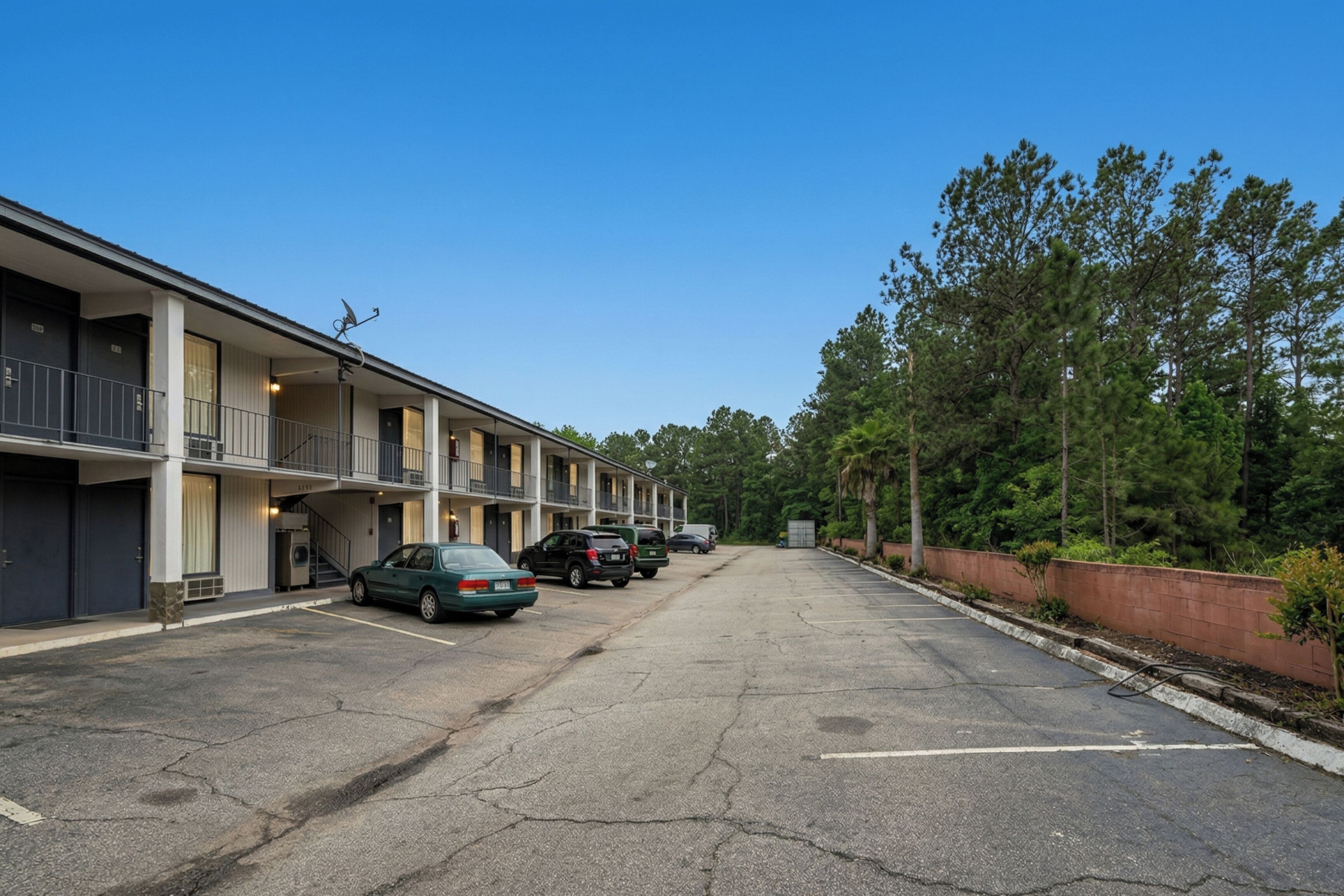 A motel with multiple floors, a parking lot, and a row of trees in the background.