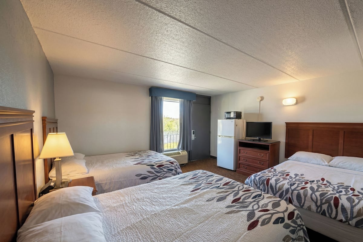 Une chambre d’hôtel avec deux lits, un bureau, une télévision et une fenêtre avec des rideaux.