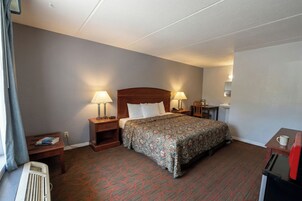 Una habitación de hotel con una cama, dos mesitas de noche con lámparas, un escritorio pequeño con una silla y un radiador.