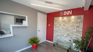 Un vestíbulo de hotel con una pared roja, una pared decorativa de piedra, un banco de vidrio y una planta en maceta.