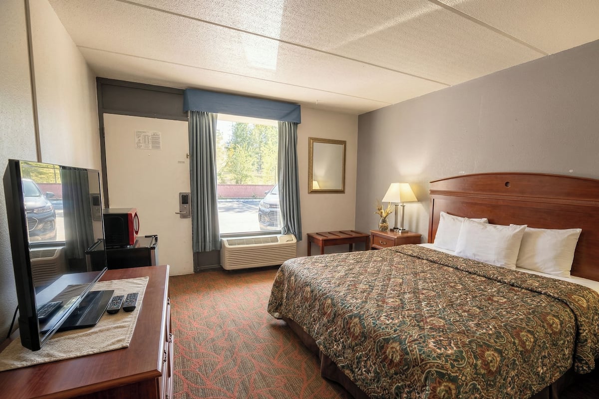 Une chambre d’hôtel avec un lit, un bureau avec un ordinateur, une télévision et une fenêtre avec des rideaux.