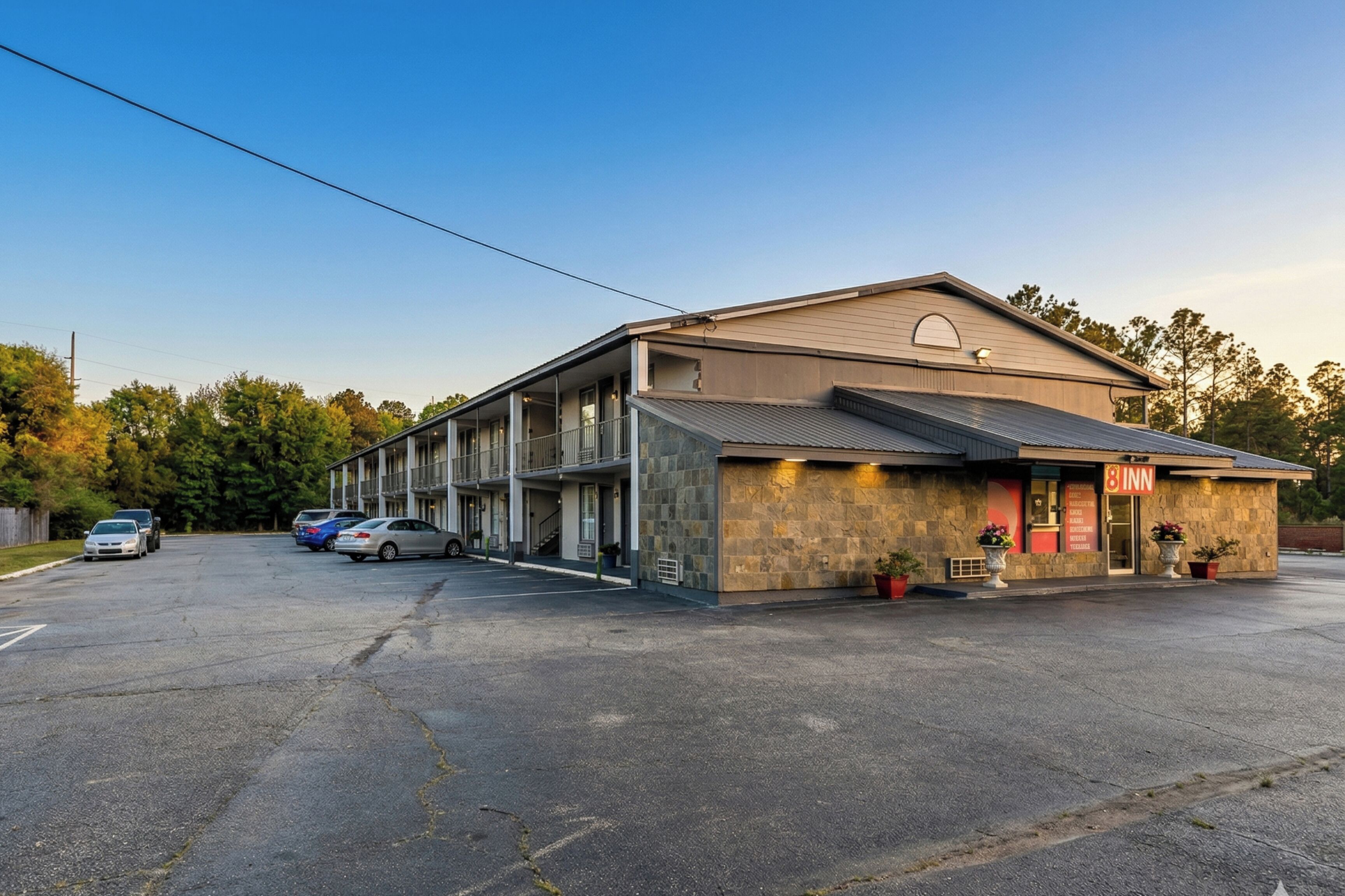 Un motel à la façade en pierre, doté de nombreux espaces de stationnement et offrant une vue sur un ciel dégagé.