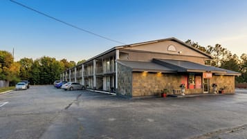 Un motel à la façade en pierre, doté de nombreux espaces de stationnement et offrant une vue sur un ciel dégagé.
