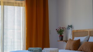 A bedroom with a bed, a bedside table with a lamp, a window with curtains, and a potted plant. - Appartement T3 bas de Villa (Vero)