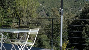 A table with a green umbrella, a metal chair, and a view of a mountainous landscape. - Appartement T3 bas de Villa (Vero)