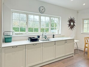 A kitchen with white cabinets, a large window, a clock, and a decorative mirror.