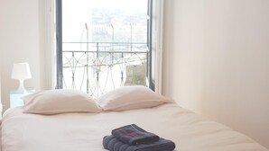 A bed with a white mattress and pillows, a folded blanket, and a view of a balcony with metal railings. - Inviting 2-bed Apartment in Porto (Porto)