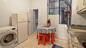 A compact kitchen with a washing machine, a small dining table with orange chairs, and a window with a view of a chimney. - Inviting 2-bed Apartment in Porto (Porto)