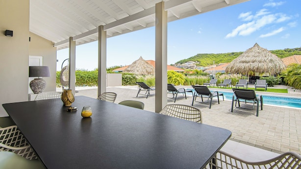 A covered outdoor area with a pool, lounge chairs, and a table with decorative items.