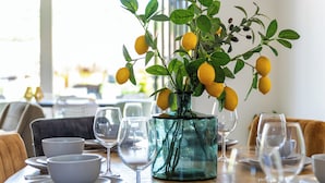 A dining table set with white bowls, plates, and wine glasses, and a vase with yellow lemons.