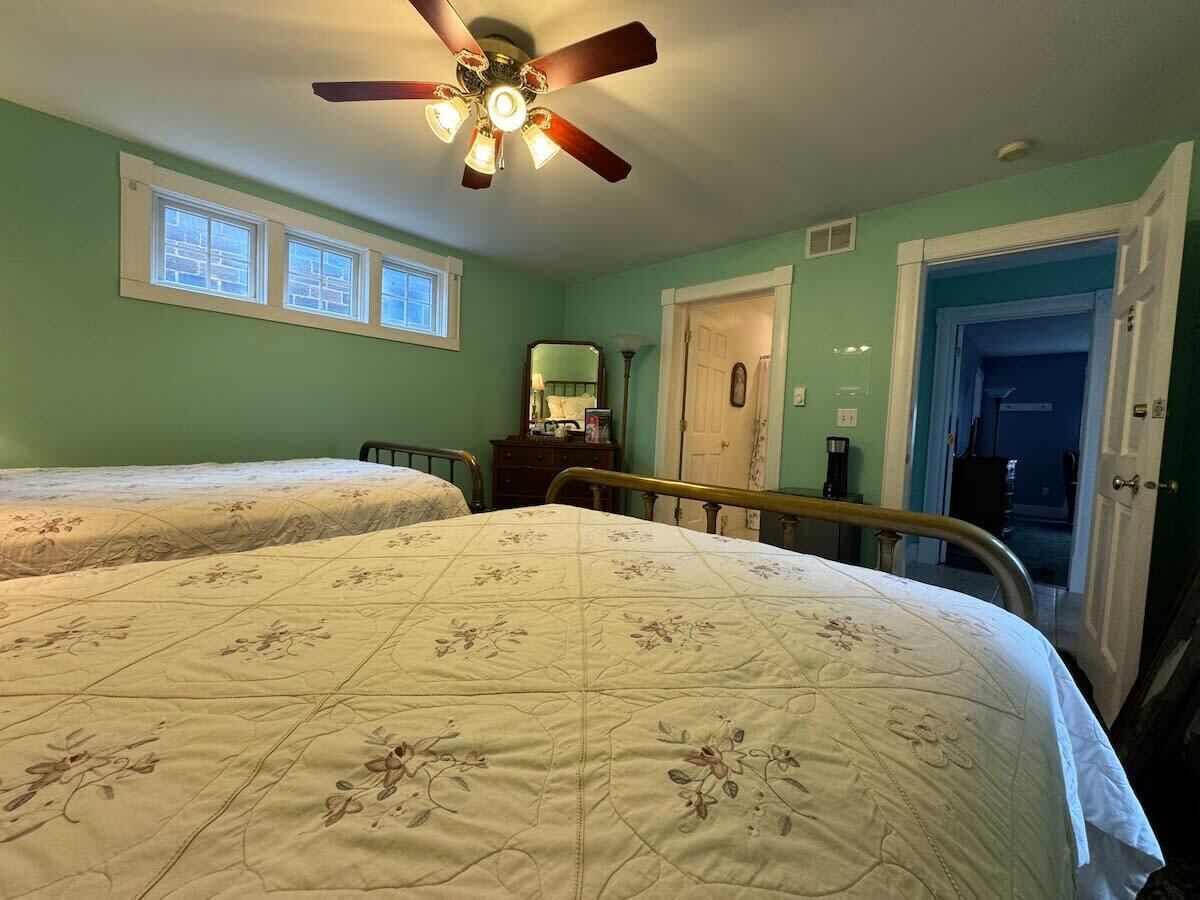 A bedroom with two beds, a ceiling fan, a dresser, a mirror, and a door leading to another room.