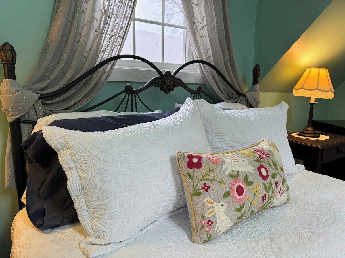 Una cama con sábanas blancas, almohadas decorativas, un cabecero de metal oscuro y una lámpara de noche.