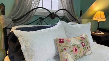 Una cama con sábanas blancas, almohadas decorativas, un cabecero de metal oscuro y una lámpara de noche.