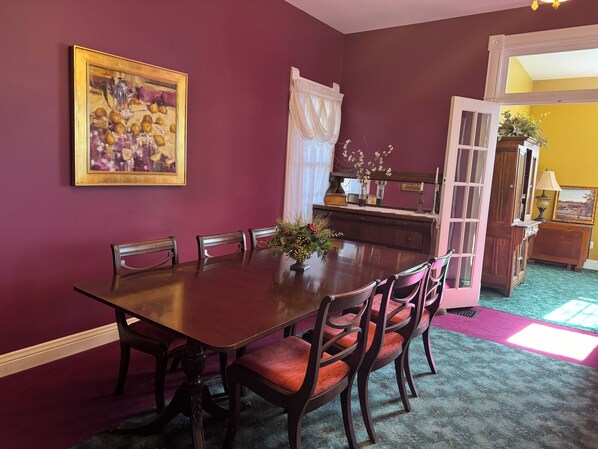 A dining room with a wooden table and chairs, a painting on the wall, and a door leading to another room. - The Wen Inn formerly Andor Wenneson (Peterson)