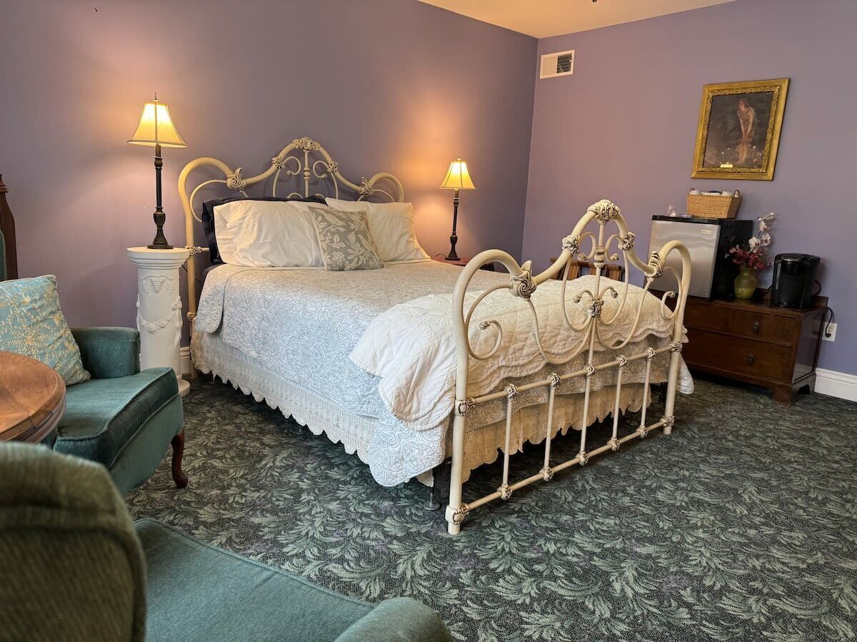 Ein Schlafzimmer mit einem bettenstilmöbel im Vintage-Look, zwei Nachttischlampen, einem kleinen Tisch und einem Stuhl.
