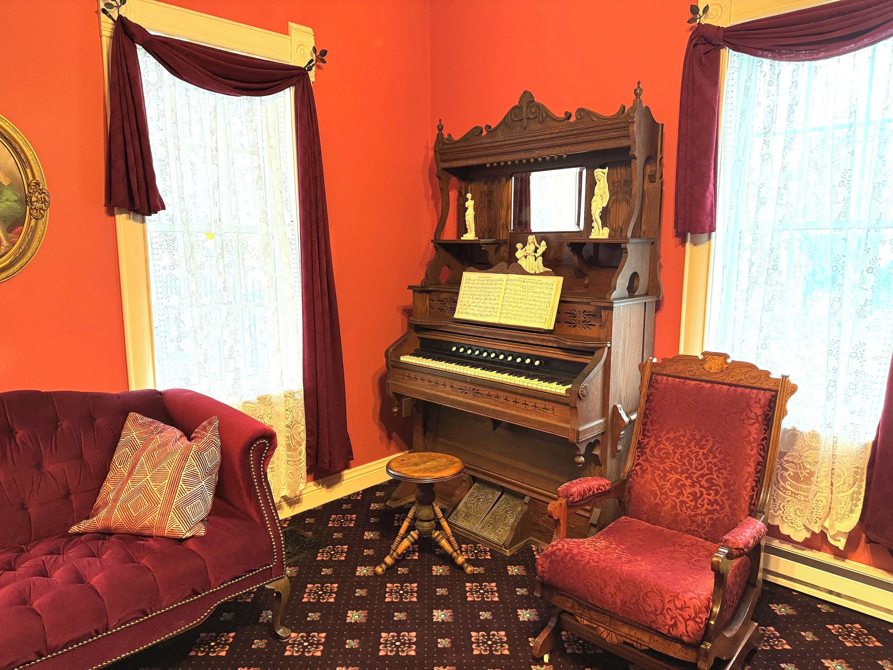 Una habitación con un piano de cola, un sofá tapizado en rojo y un sillón a juego.