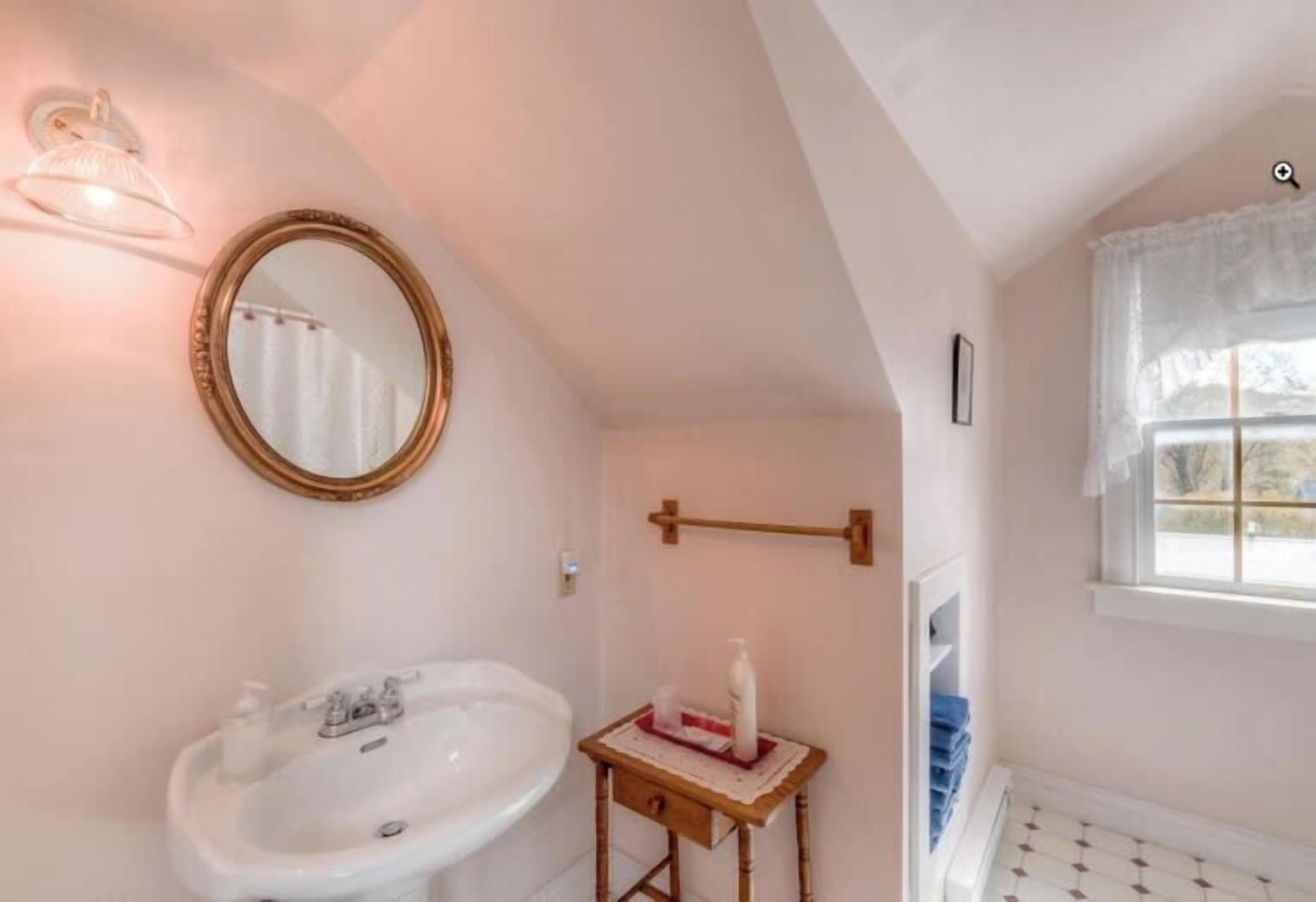 A bathroom with a white sink, a mirror, a towel rack, and a window with a view.
