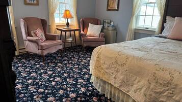 Una habitación con una cama, dos sillones, una mesita con lámpara y una mesita de noche.