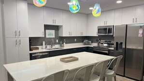 Una cucina moderna con mobili bianchi, un'isola centrale, elettrodomestici in acciaio inossidabile e lampade a sospensione colorate.