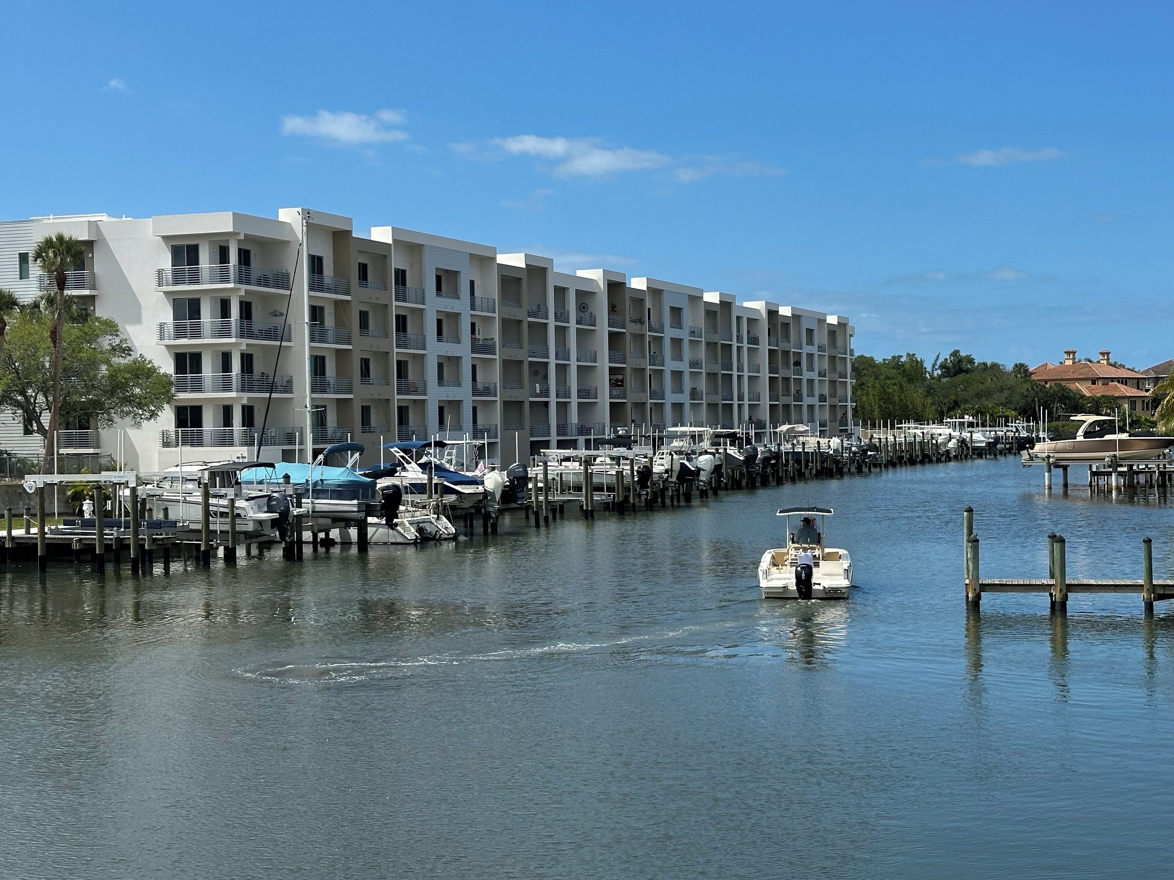 A marina with boats docked, a modern building with balconies, and a clear blue sky.