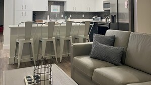 Una cucina moderna con mobili bianchi, un'area pranzo con sedie bianche e un divano con un cuscino.