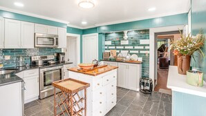 A modern kitchen with white cabinets, a central island, stainless steel appliances, and teal backsplash tiles. - Experience a 17th-Century Spring Manor (Eagleville)
