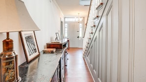 A hallway with a wooden floor, a lamp, framed artwork, and a staircase with white railings. - Experience a 17th-Century Spring Manor (Eagleville)