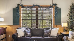 A cozy living room with a brown leather sofa, a round coffee table, and a window with shutters. - 2BD Cabin, Sleeps 6, near Hwy 76, Tanger Outlets- DISCOUNT TICKETS! (Branson)