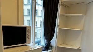 Une petite cuisine avec un réfrigérateur blanc, un four à micro-ondes et une fenêtre donnant sur les bâtiments environnants.