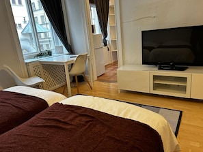 A hotel room with two beds, a TV, a desk with a chair, and a view of the city.