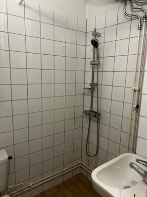 A bathroom with white tiled walls, a shower with a handheld showerhead, a white sink with a chrome faucet, and a toilet.