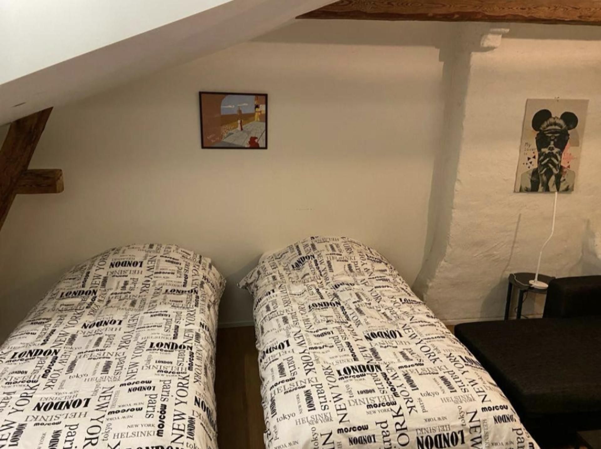 Quarto com duas camas, um pequeno quadro e um cartaz na parede.