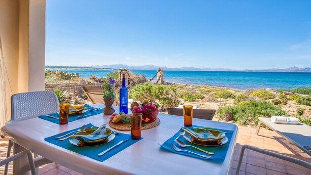 An outdoor dining table set with plates, cutlery, and glasses, overlooking a coastal landscape with mountains in the distance. - Villa in front of the sea Casa Sa Nau in Mallorca (Arta)