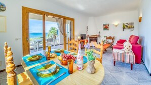A dining area with a table set for four, a wooden chair, a red sofa, and a view of the sea through a glass door. - Villa in front of the sea Casa Sa Nau in Mallorca (Arta)