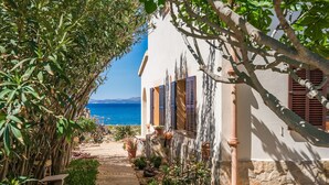 A coastal building with a stone pathway leading to a door, surrounded by greenery and overlooking the sea. - Villa in front of the sea Casa Sa Nau in Mallorca (Arta)