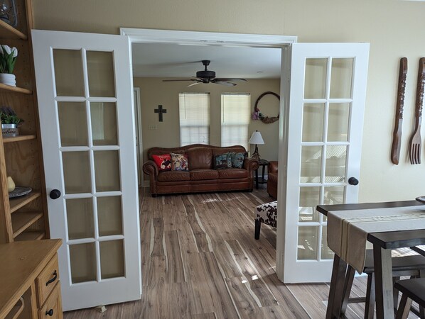 An open door leading to a living room with a brown leather sofa, a small table, and a ceiling fan.