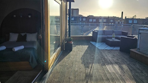 A rooftop terrace with a bed, seating area, and a city view.