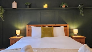 A neatly made bed with white linens, a green throw pillow, and two bedside lamps.
