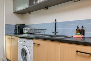 A compact kitchen with a washing machine, a coffee maker, a toaster, and a sink. - Calming Sea View City Apartment (Edinburgh)