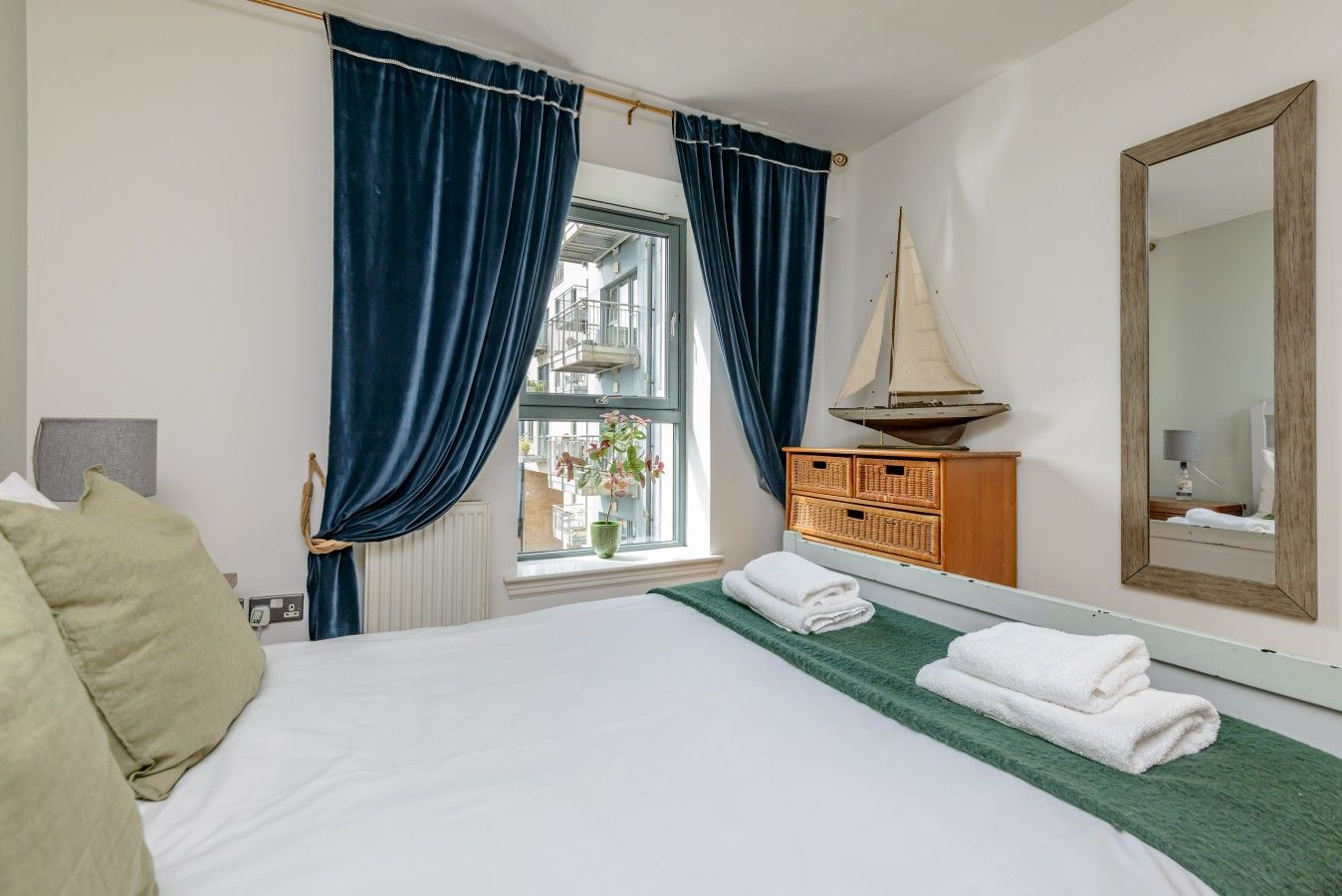 Hotellihuone, jossa on sänky, lipasto, ikkuna verhoilla, purjelaivamainen koriste ja peili.